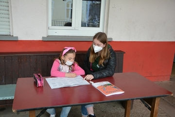 Lina Schulte (rechts) unterstützt vor der Don Bosco Halle in Trier-West die achtjährige Fabienne bei den Hausaufgaben.